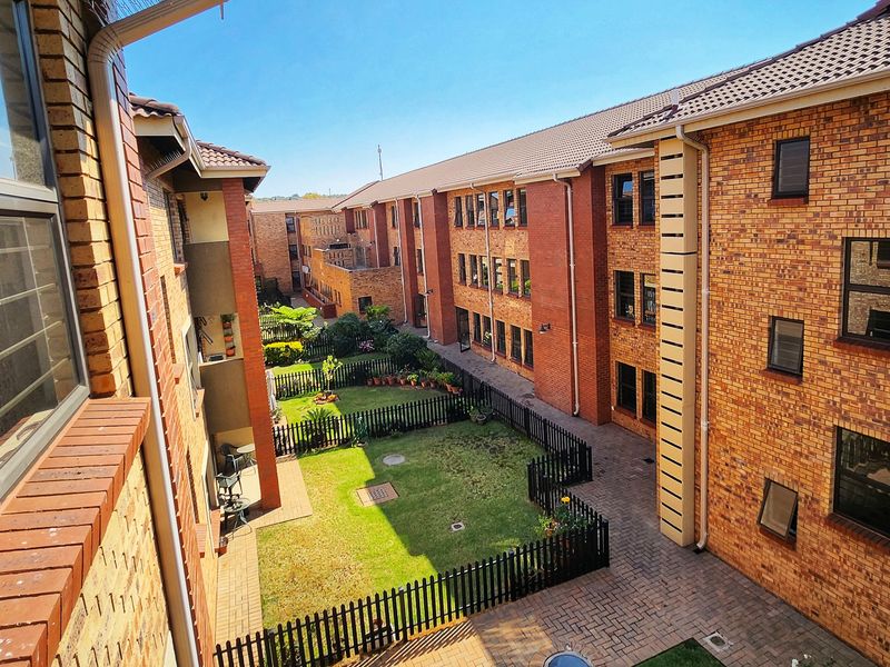 An elevated view of the apartment complex courtyard featuring face brick buildings, a central landscaped garden, and paved walkways.