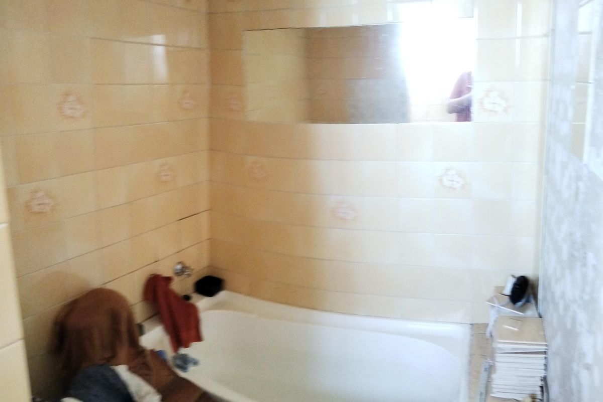 A bathroom featuring a built-in bathtub with cream-colored wall tiles and a wall-mounted mirror, currently undergoing renovation or maintenance.