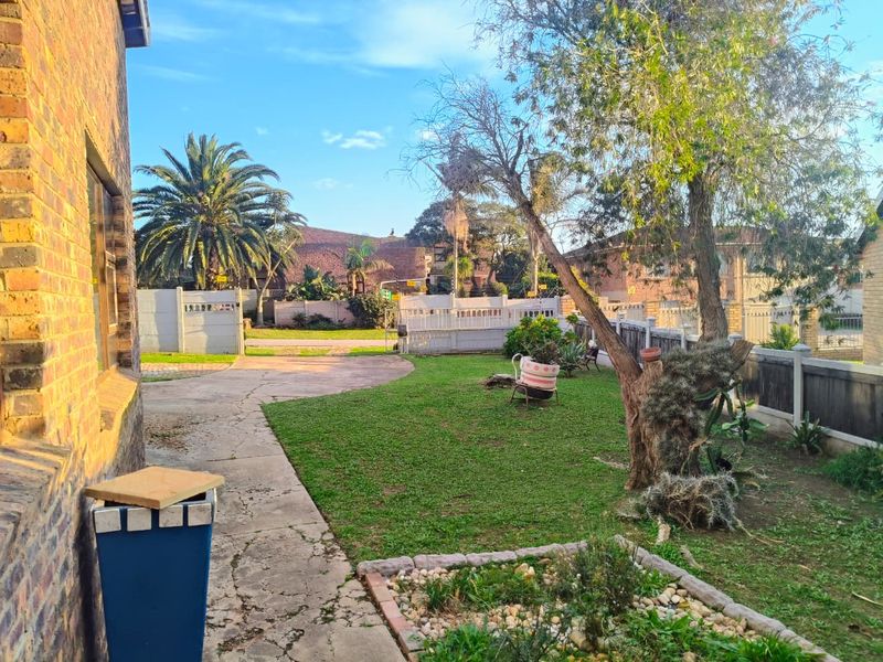 A view of the property's front garden and driveway, featuring a brick facade, paved walkway, and established trees.