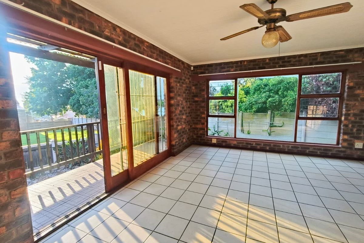 Spacious living area featuring exposed brick walls, tiled flooring, a ceiling fan, and large sliding doors providing direct access to the outdoor patio.