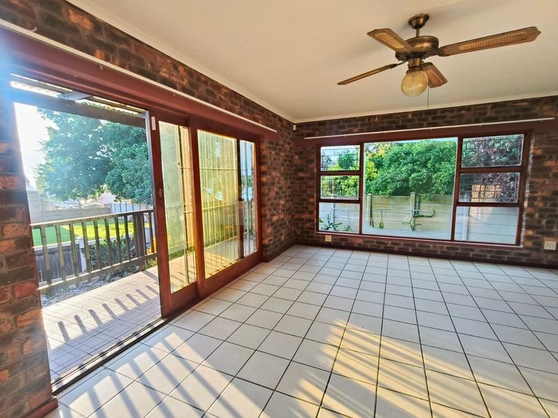 Spacious living area featuring exposed brick walls, tiled flooring, a ceiling fan, and large sliding doors providing direct access to the outdoor patio.