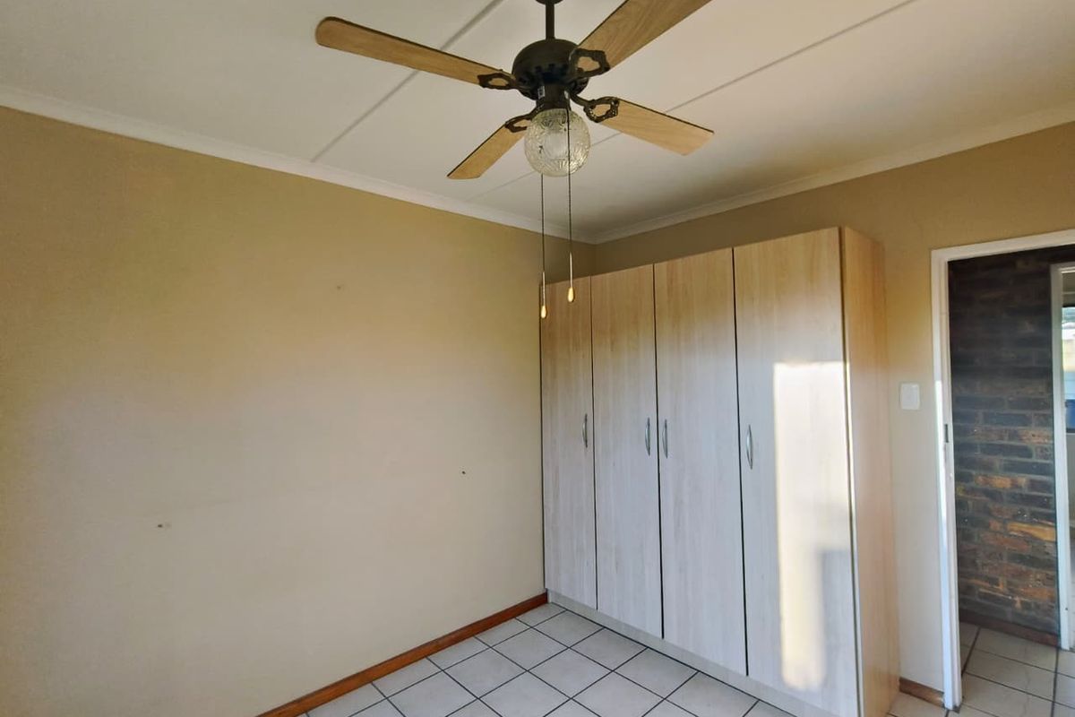A bedroom featuring built-in wooden cupboards, tiled flooring, and a ceiling fan, offering a functional and neutral living space.