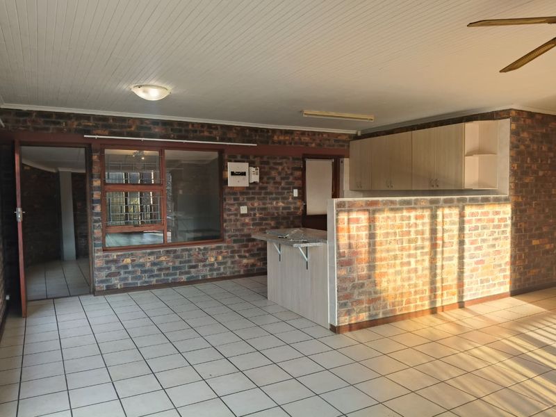 Open plan living area featuring exposed brick walls, tiled flooring, and a functional kitchen counter with overhead cabinetry.