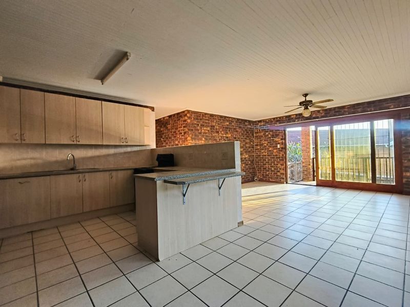 Open-plan kitchen and living area featuring tiled flooring, built-in cabinetry, breakfast counter, and sliding glass doors leading to an outdoor patio.