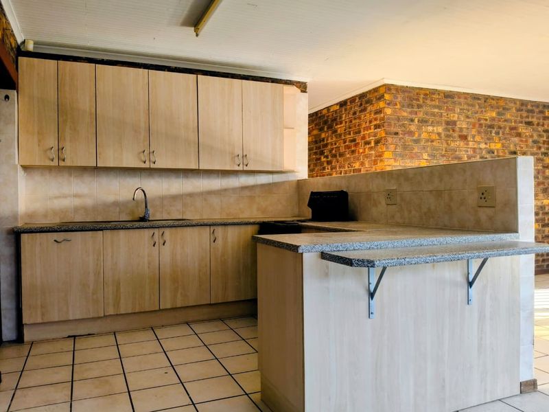 A functional kitchen featuring light wood-finish cabinetry, granite-look countertops, a breakfast bar, and tiled flooring, open to the adjacent living area.