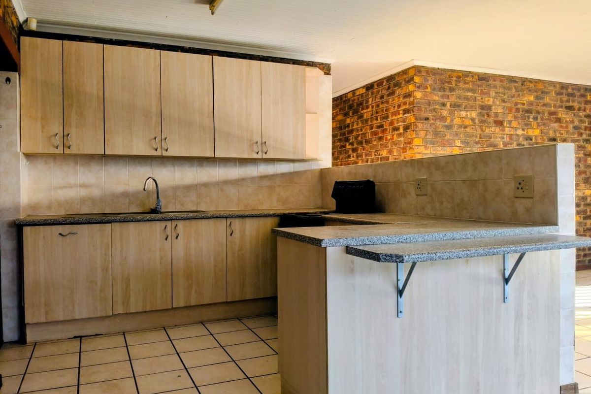 A functional kitchen featuring light wood-finish cabinetry, granite-look countertops, a breakfast bar, and tiled flooring, open to the adjacent living area.