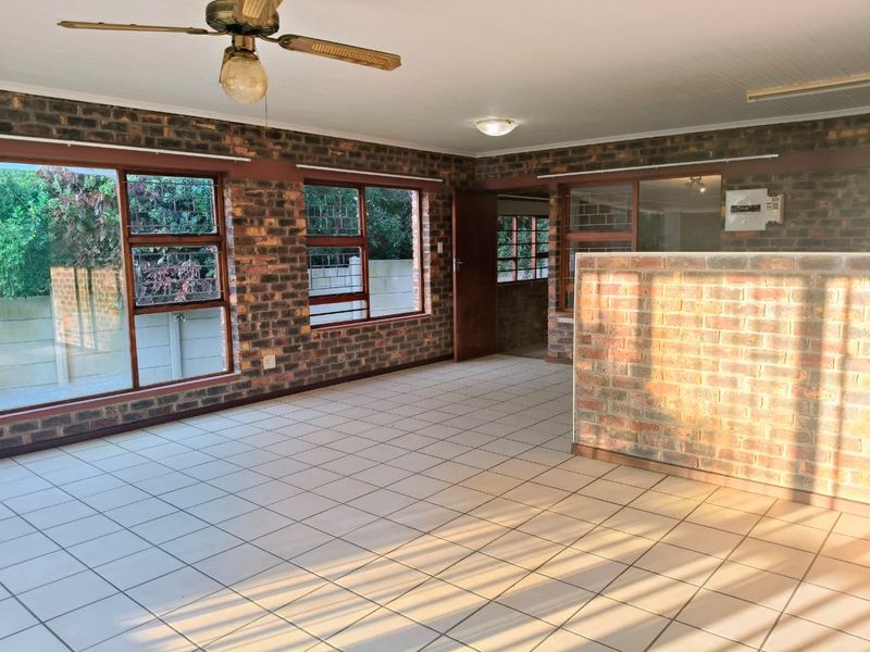 Spacious open-plan living area featuring exposed brick walls, large windows, tiled flooring, and a ceiling fan.