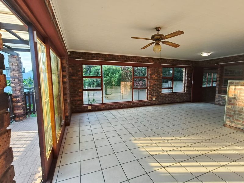 Spacious living area featuring exposed face-brick walls, large windows, tiled flooring, and a ceiling fan, offering a bright and open atmosphere.