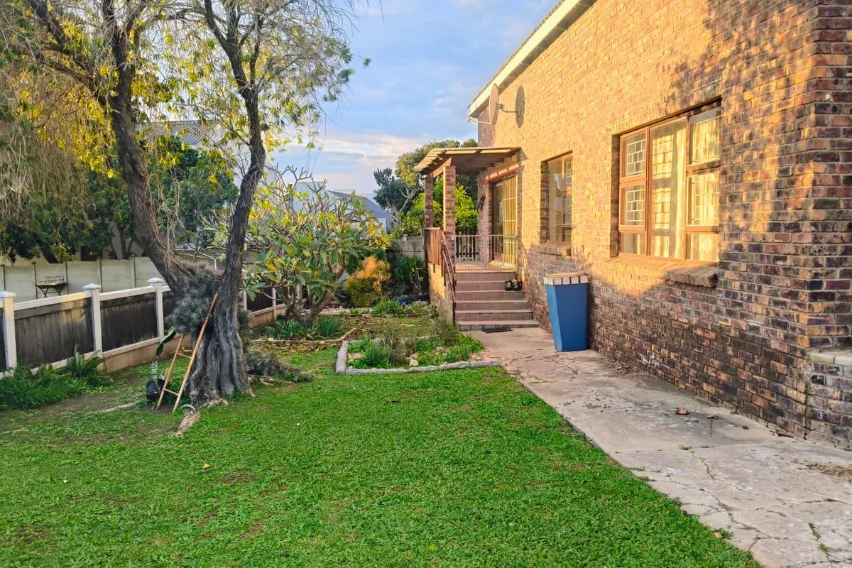 Rear view of the house featuring a brick facade, a small covered patio with stairs, and a garden area with lawn and mature trees.
