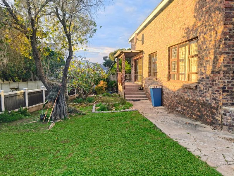 Rear view of the house featuring a brick facade, a small covered patio with stairs, and a garden area with lawn and mature trees.