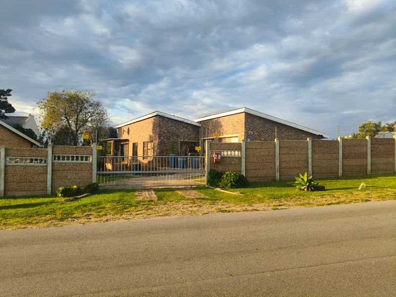A single-story face-brick house featuring a secure perimeter wall, metal entrance gate, and a paved driveway, set within a residential street.