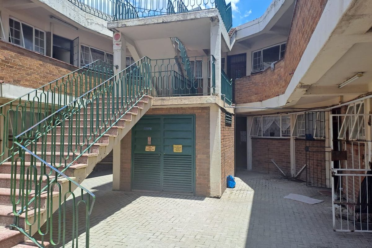 Exterior view of a multi-level apartment complex courtyard featuring brick facade, external staircases with metal railings, and paved ground level access.