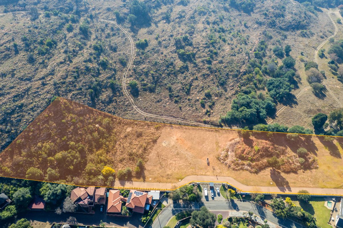 Aerial view of a vacant residential plot featuring natural landscape, hillside terrain, and established boundary lines within a residential estate.