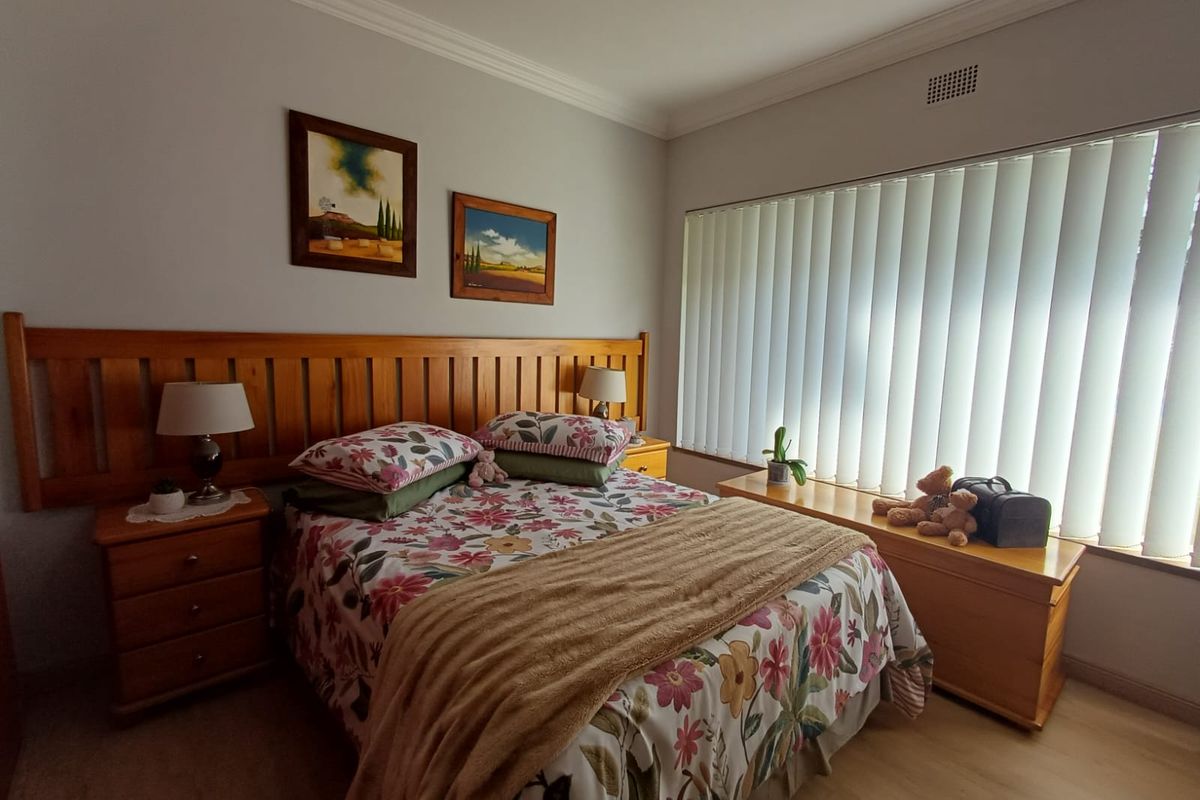 A well-maintained bedroom featuring a built-in wooden headboard, neutral wall finishes, and vertical window blinds.