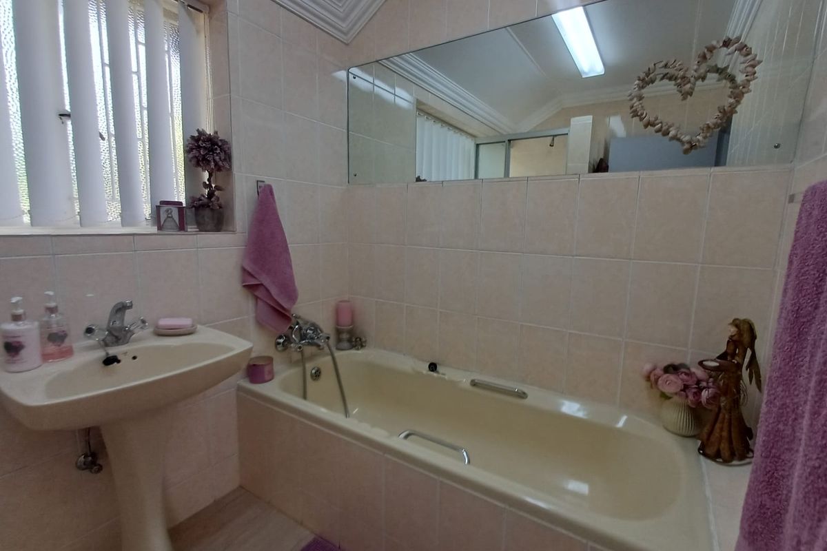 A functional bathroom featuring a pedestal basin, a built-in bathtub with shower mixer, and wall-to-wall vanity mirror with neutral tiling.