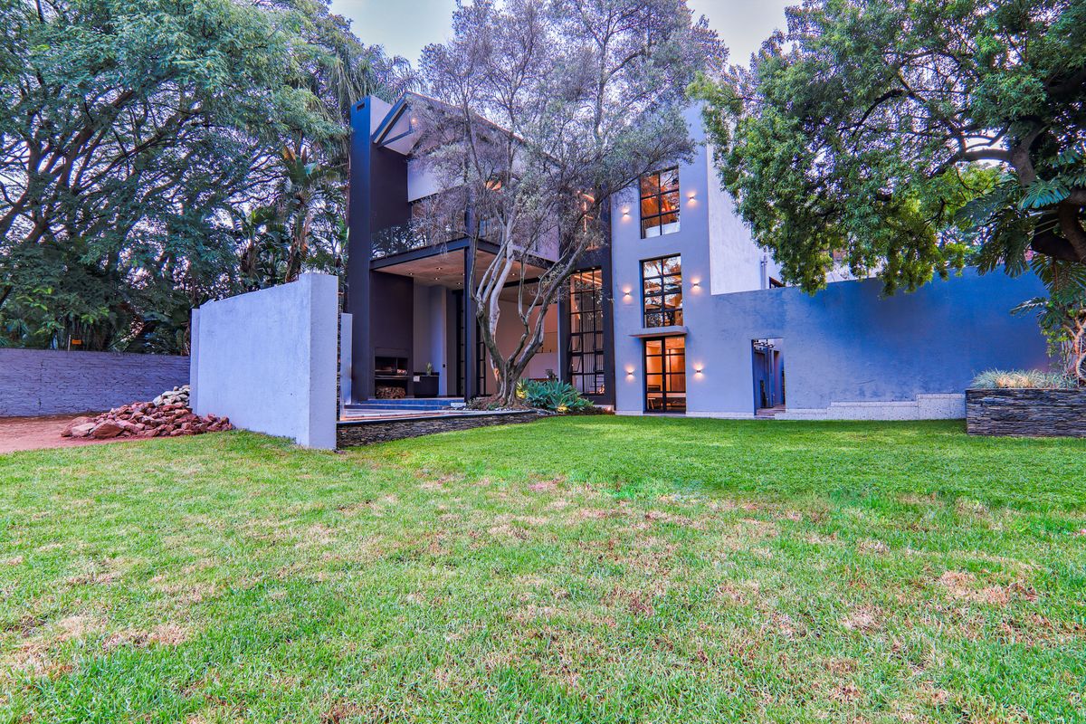 Modern multi-story architectural home featuring a sleek facade, large glass windows, and a spacious landscaped rear garden with mature trees.