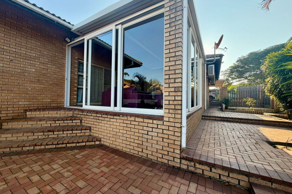 A well-maintained brick exterior featuring a paved patio area and a sunroom with large sliding glass doors.