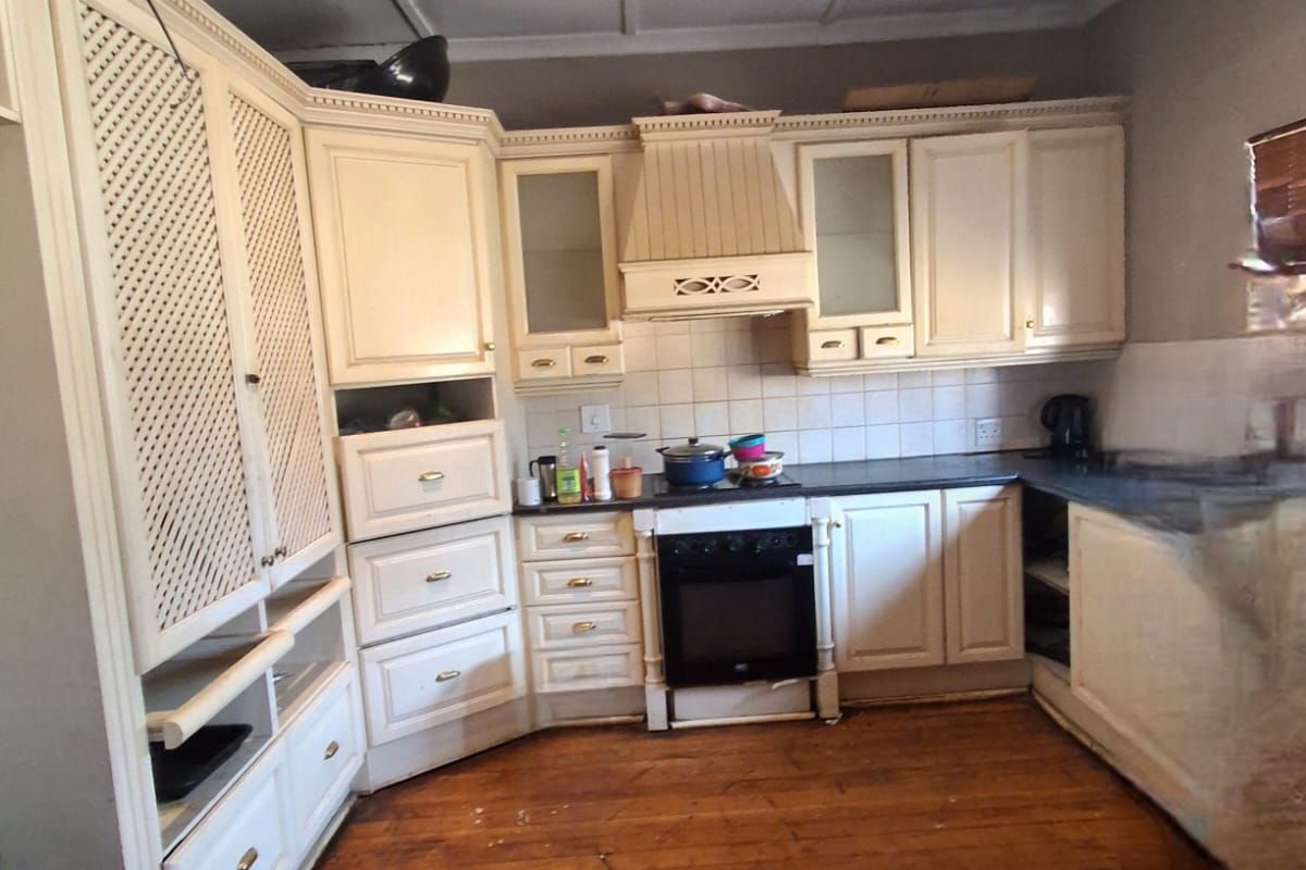 A traditional kitchen featuring cream-toned cabinetry, integrated oven and extractor fan, tiled backsplash, and original timber flooring.