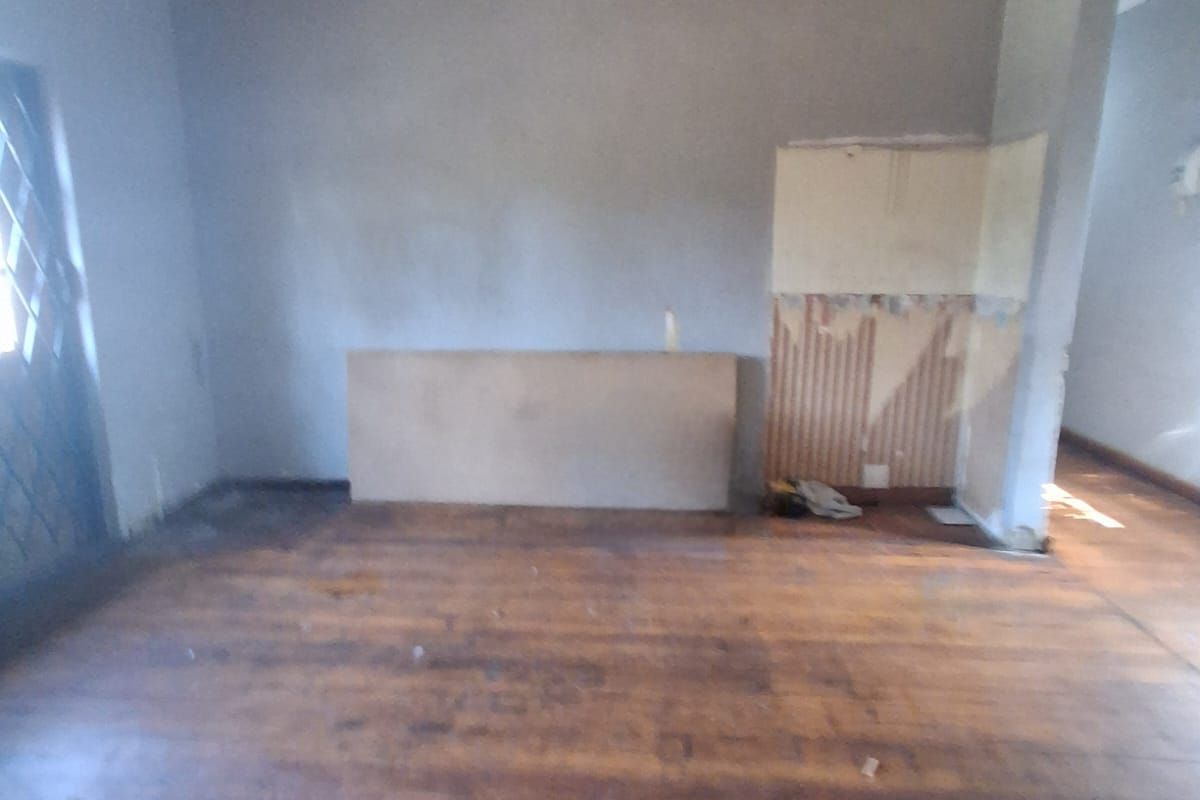 An empty living room featuring original timber flooring and a timber-clad ceiling, currently requiring renovation and cosmetic updates to restore its condition.