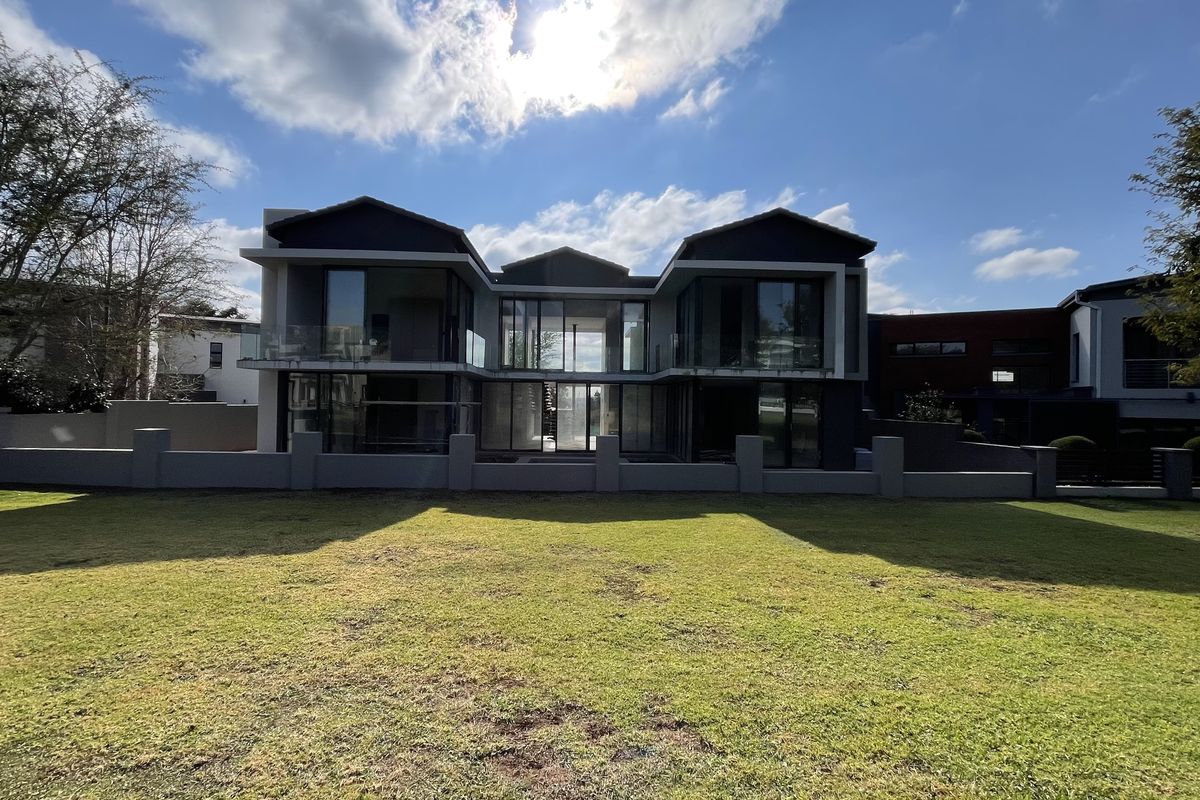 A modern double-story residential property featuring large glass facades, balconies, and a spacious manicured lawn in the rear garden area.