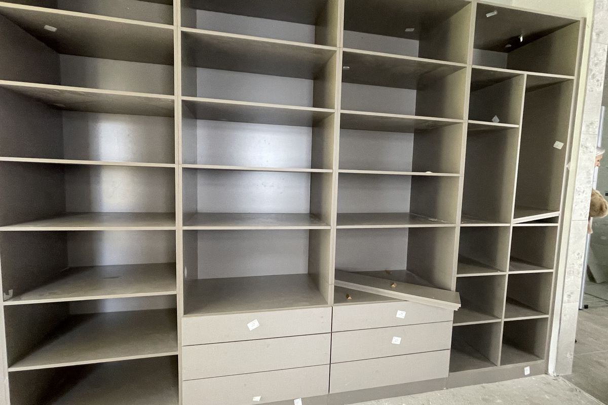 A large built-in walk-in closet storage unit featuring multiple open shelving compartments and lower drawers, currently showing signs of damage and incomplete installation.