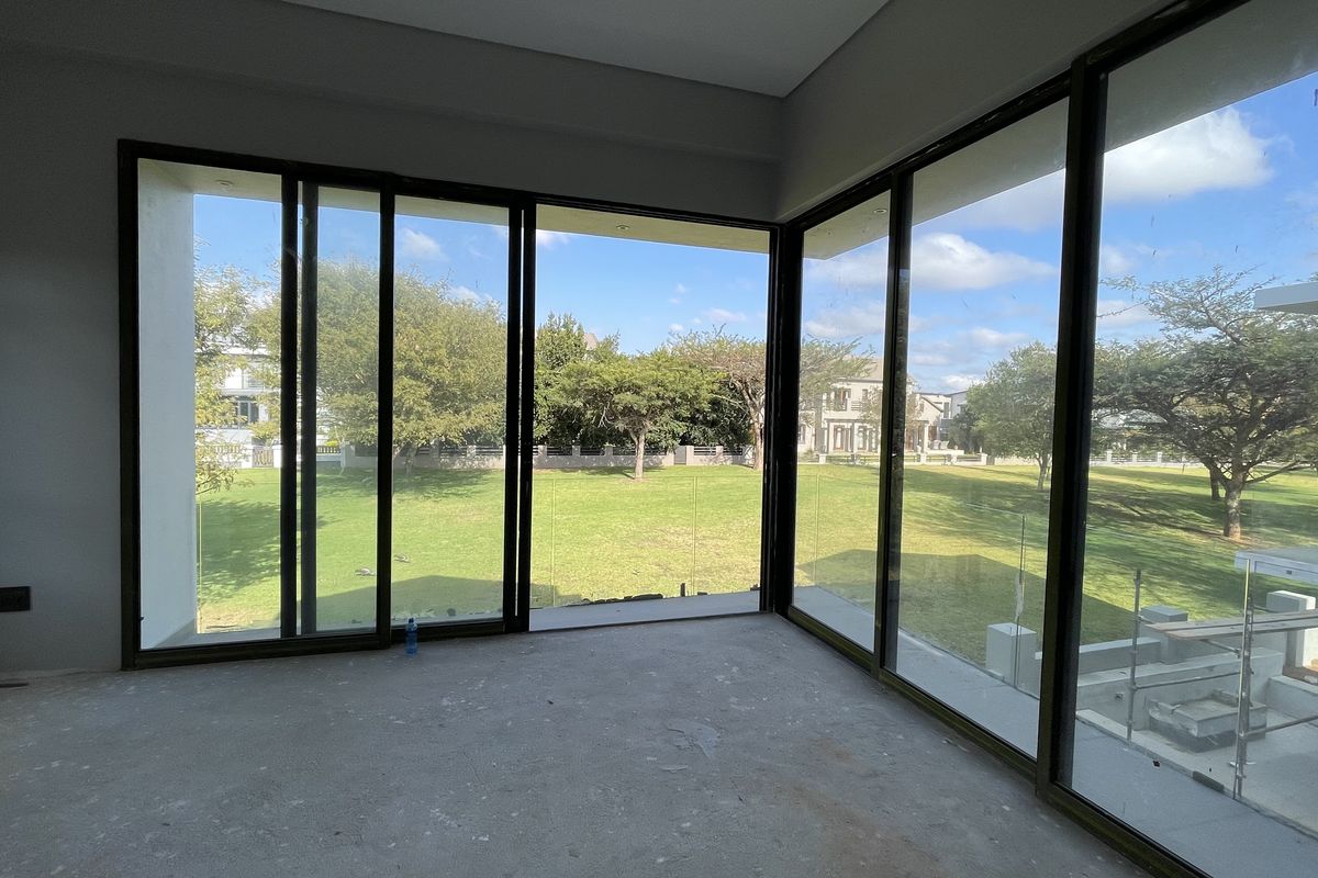 An empty, unfinished living area featuring expansive floor-to-ceiling sliding glass doors that provide abundant natural light and views of the surrounding garden.