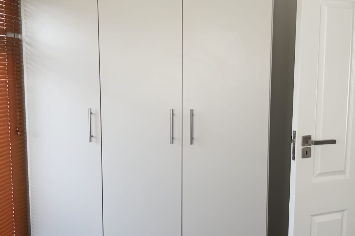 A bedroom featuring a built-in wardrobe with modern white cabinetry and sleek metal handles, complemented by tiled flooring and a panelled door.