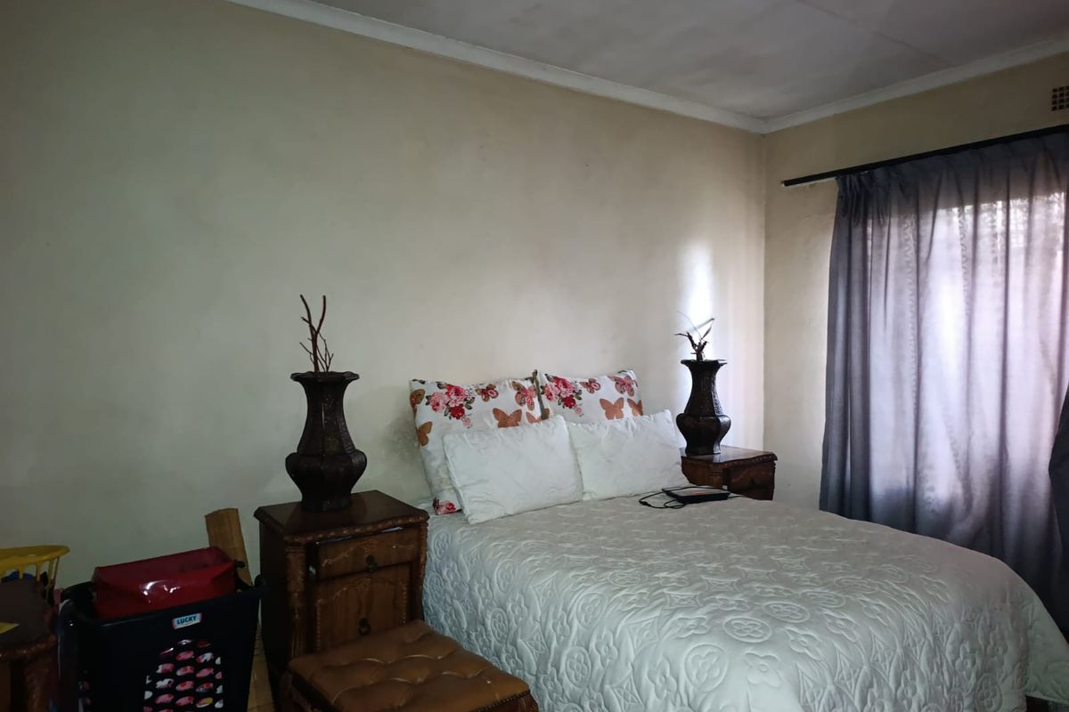 A standard bedroom featuring neutral wall finishes, a ceiling with visible wear, and a window fitted with curtain rails.