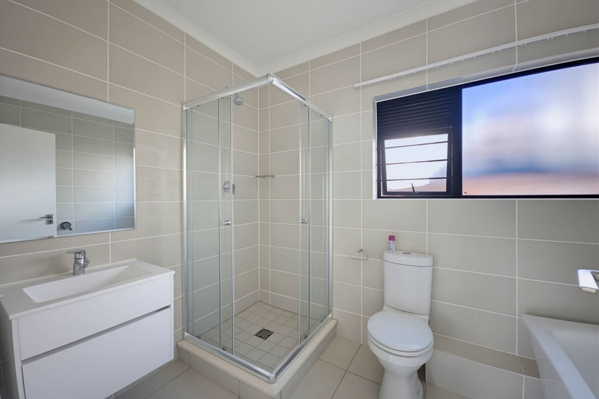 Modern bathroom featuring a glass-enclosed shower, wall-mounted vanity with basin, and a white toilet, finished with neutral floor-to-ceiling wall tiles.