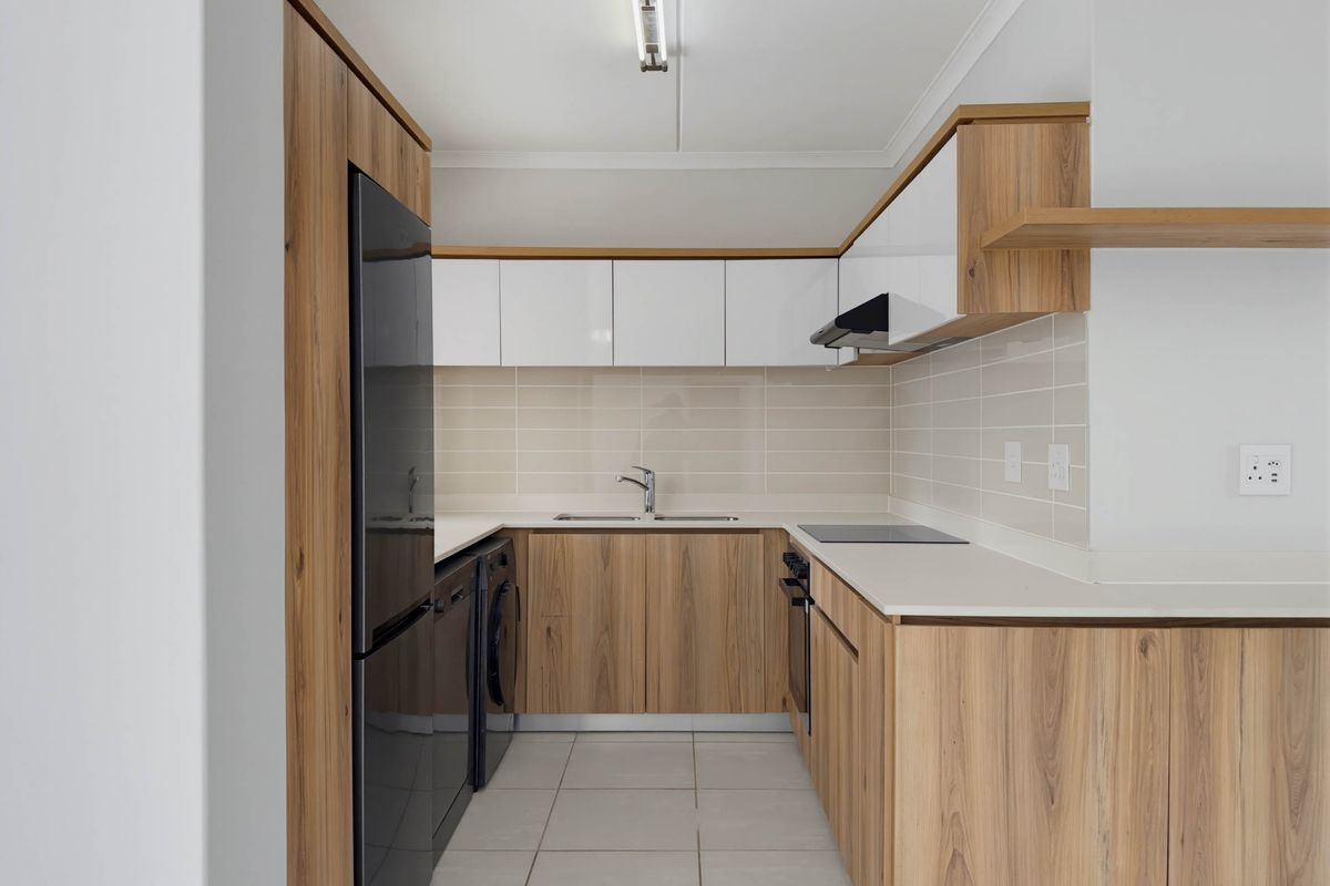 Modern kitchen featuring wood-grain cabinetry, white upper cabinets, stone countertops, integrated hob, oven, and extractor fan with tiled splashback.