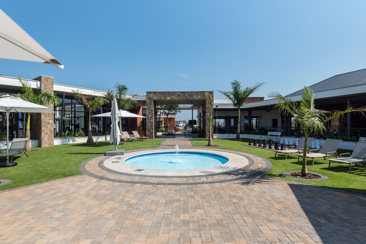 A well-maintained communal courtyard featuring a central circular fountain, paved walkways, manicured lawn, and surrounding building structures with stone cladding accents.