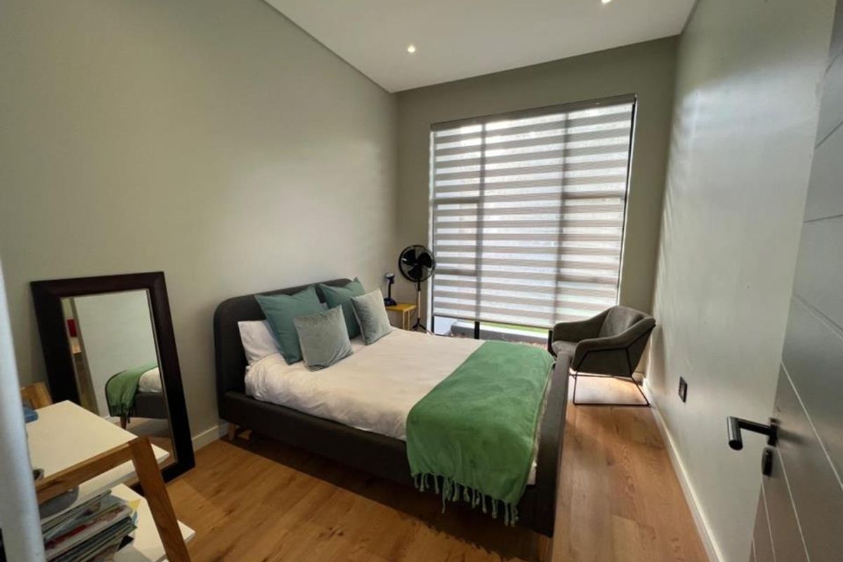 A well-lit bedroom featuring modern wood-look flooring, recessed ceiling lighting, and a large window with fitted blinds.
