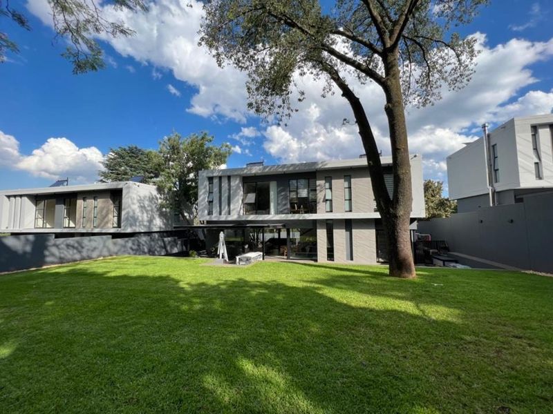 A view of the rear elevation of a modern cluster home, featuring a well-maintained lawn, mature tree, and contemporary architectural design.