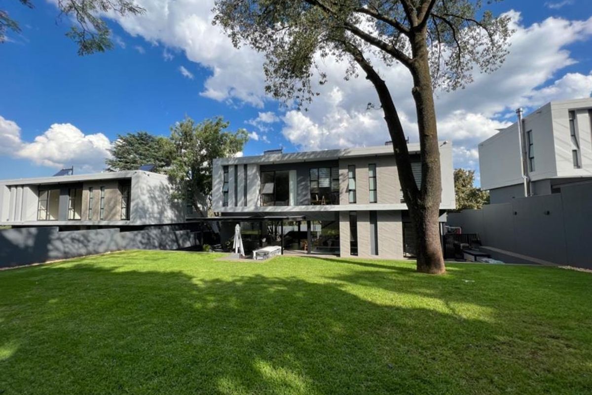 A view of the rear elevation of a modern cluster home, featuring a well-maintained lawn, mature tree, and contemporary architectural design.