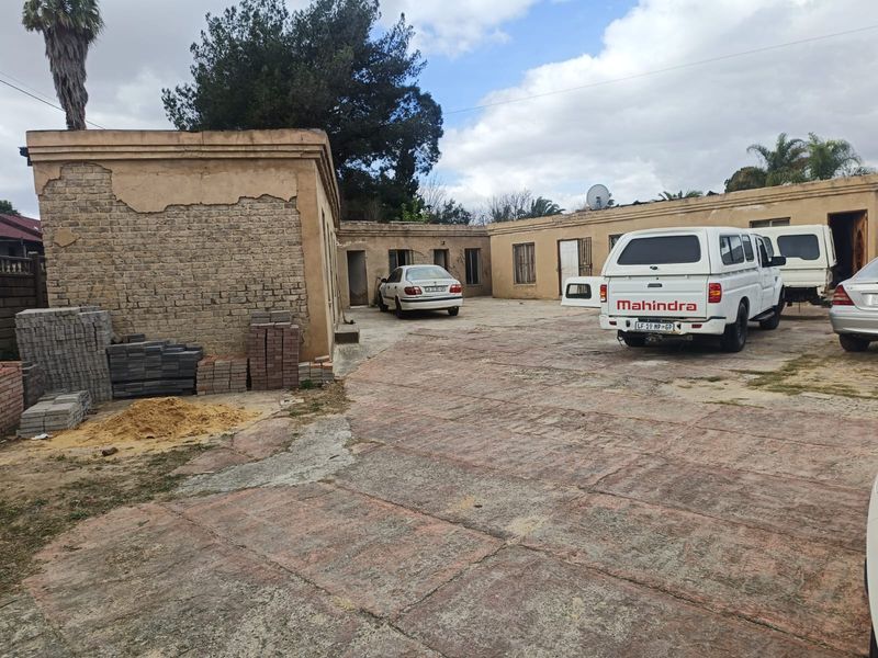 Rear exterior view of the property featuring a large paved driveway and masonry building structures requiring significant maintenance and plaster repair.