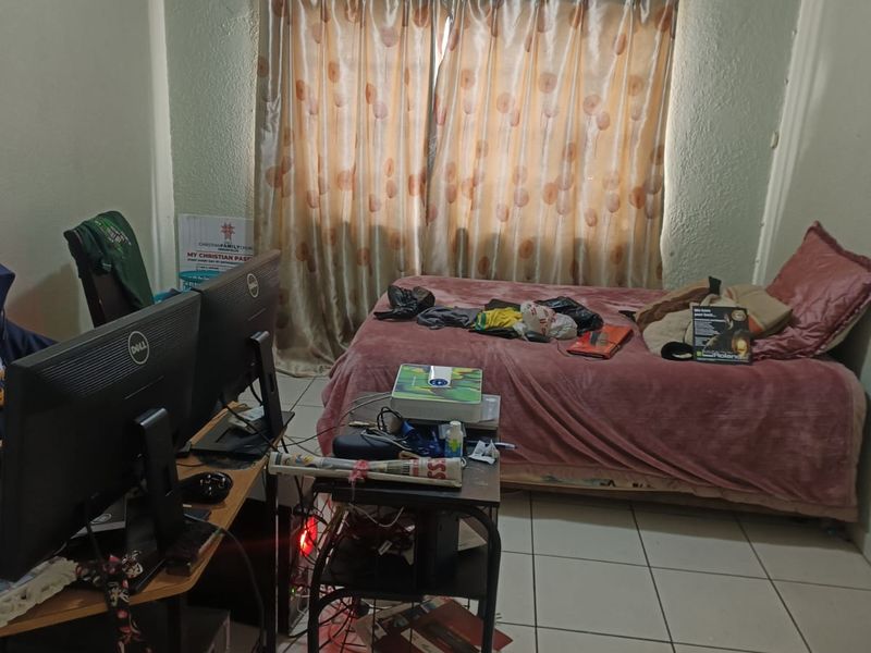 A bedroom featuring tiled flooring and a curtain rail, currently utilized as a multi-purpose living and workspace area.