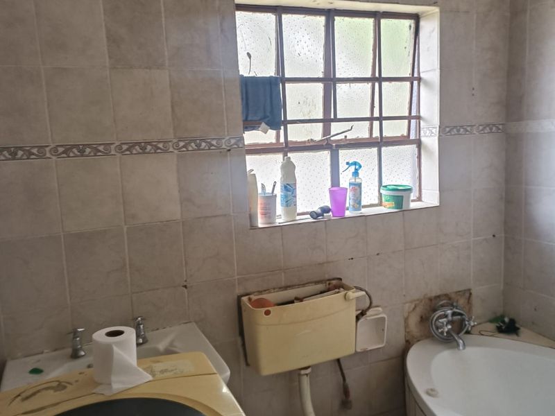 A dated bathroom featuring a built-in bathtub, pedestal basin, and wall-mounted cistern, requiring significant renovation and modernization of finishes.