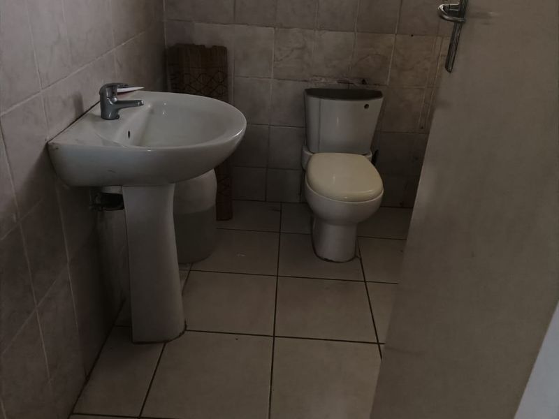 A compact bathroom featuring a pedestal basin, toilet, and neutral wall and floor tiling, requiring cosmetic updates to improve its overall condition.