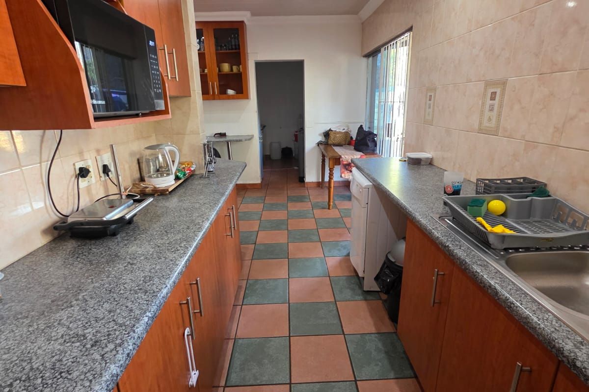 Galley-style kitchen featuring wood-veneer cabinetry, granite-look countertops, tiled splashbacks, and a checkerboard tiled floor.
