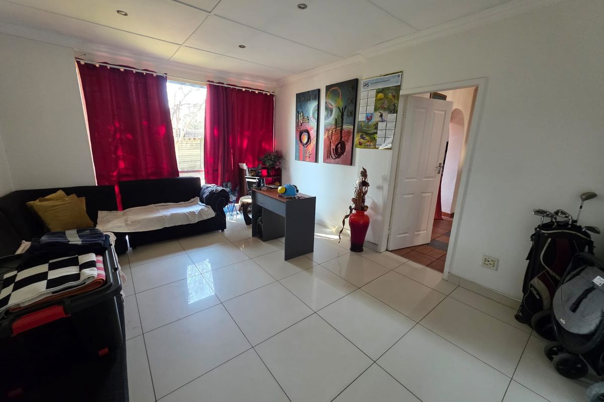A spacious living room featuring large format white floor tiles, recessed downlighting, and a neutral color palette with access to an adjoining room.