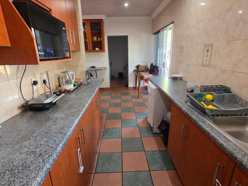 Galley-style kitchen featuring wood-veneer cabinetry, granite-look countertops, tiled splashbacks, and a checkerboard tiled floor.