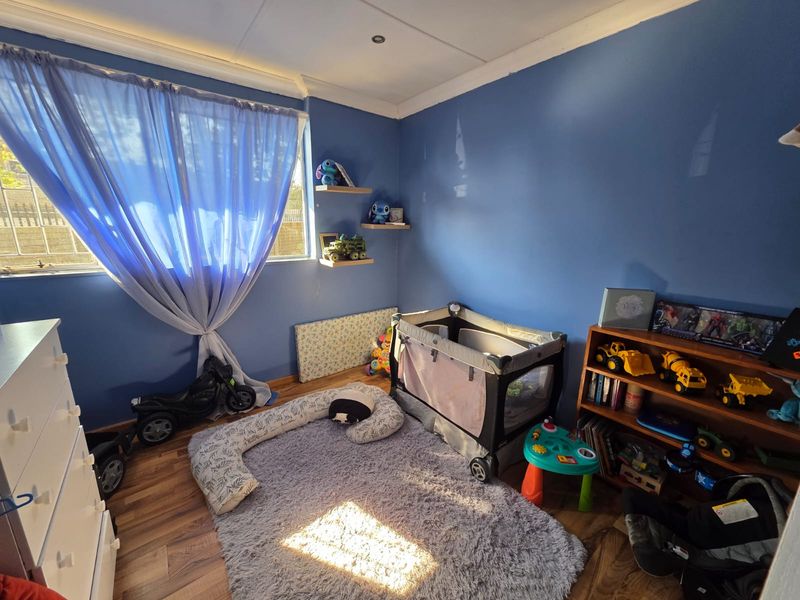 A bedroom featuring laminate flooring, blue painted walls, and built-in floating corner shelves, providing a functional space with natural light.
