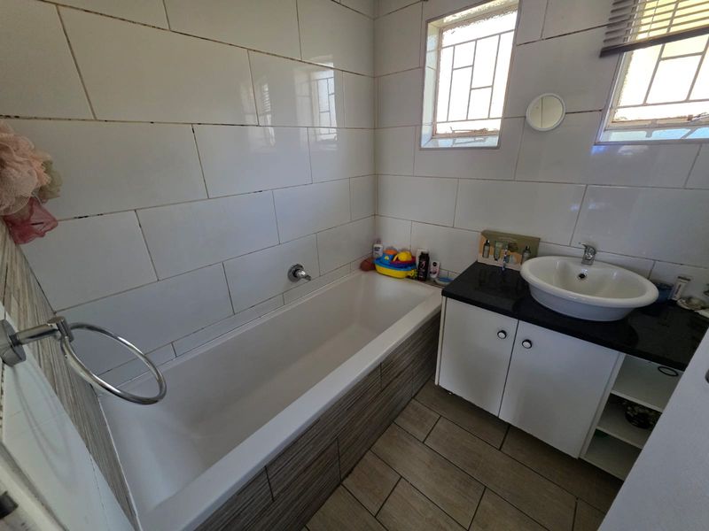 A functional bathroom featuring a built-in bathtub, a vanity cabinet with a countertop basin, and tiled wall finishes.