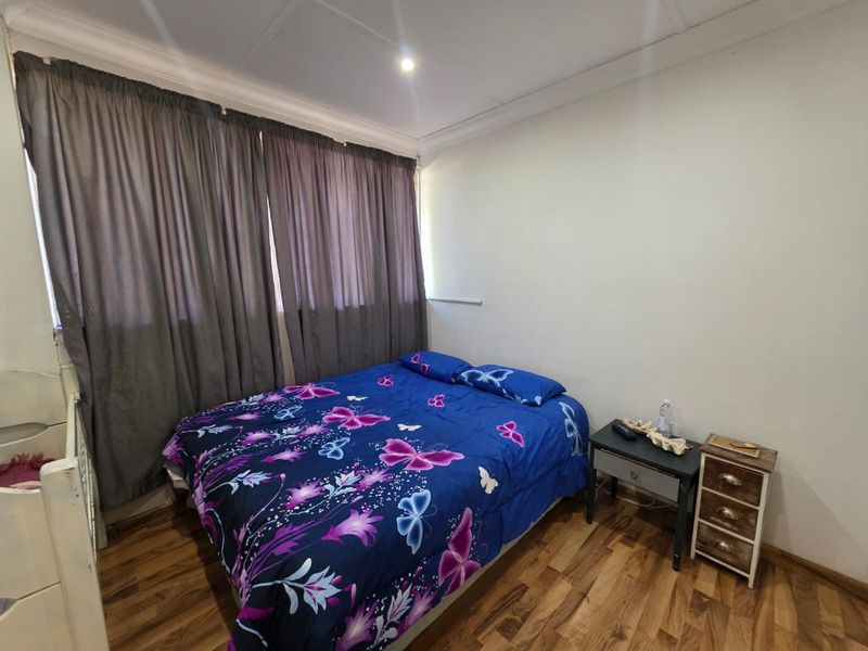 A functional bedroom featuring wood-look flooring, recessed ceiling lighting, and full-length window curtains.