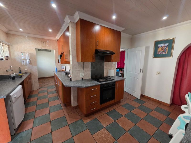 A functional kitchen featuring wooden cabinetry, granite countertops, a built-in oven with extractor fan, and tiled flooring throughout.