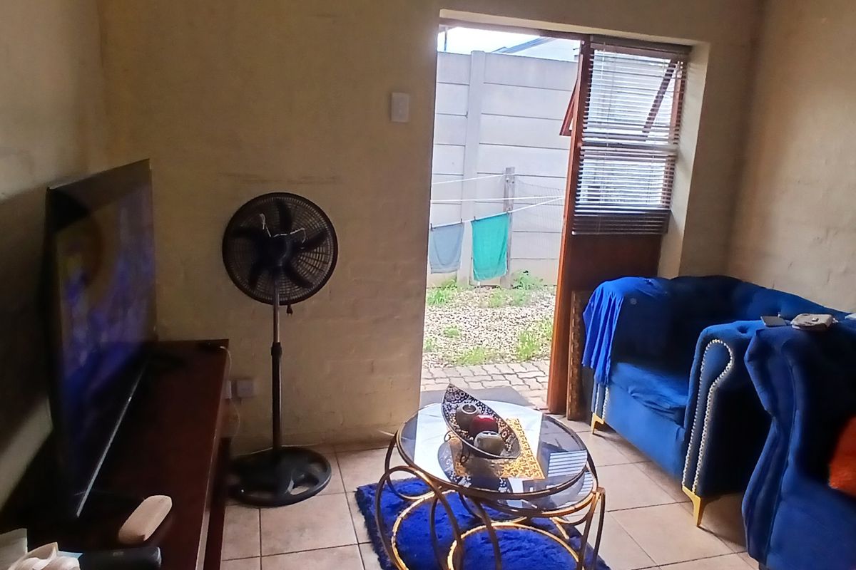 A living room area featuring tiled flooring and a door providing direct access to the exterior rear yard.