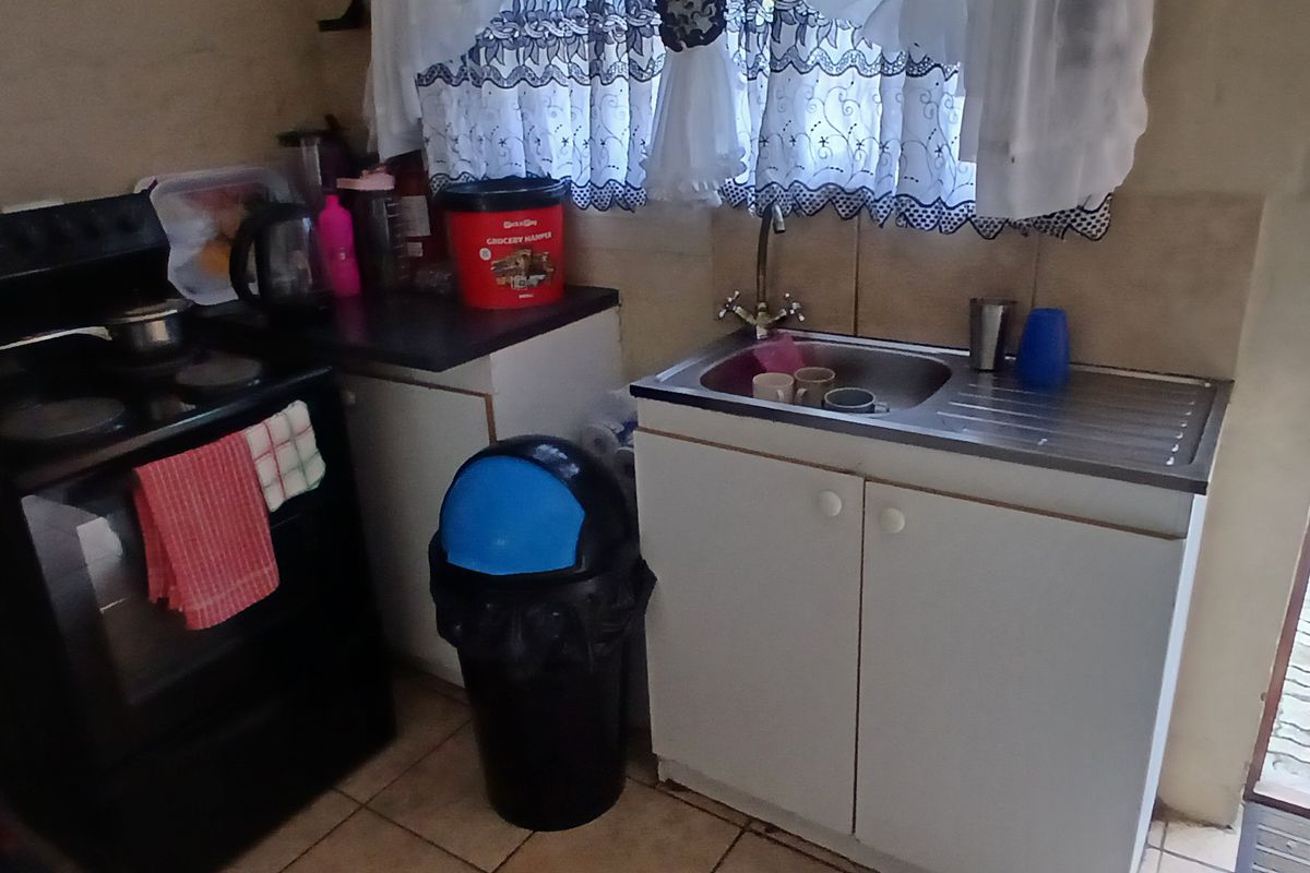 A compact kitchen area featuring a built-in sink, tiled backsplash, and space for a freestanding stove.