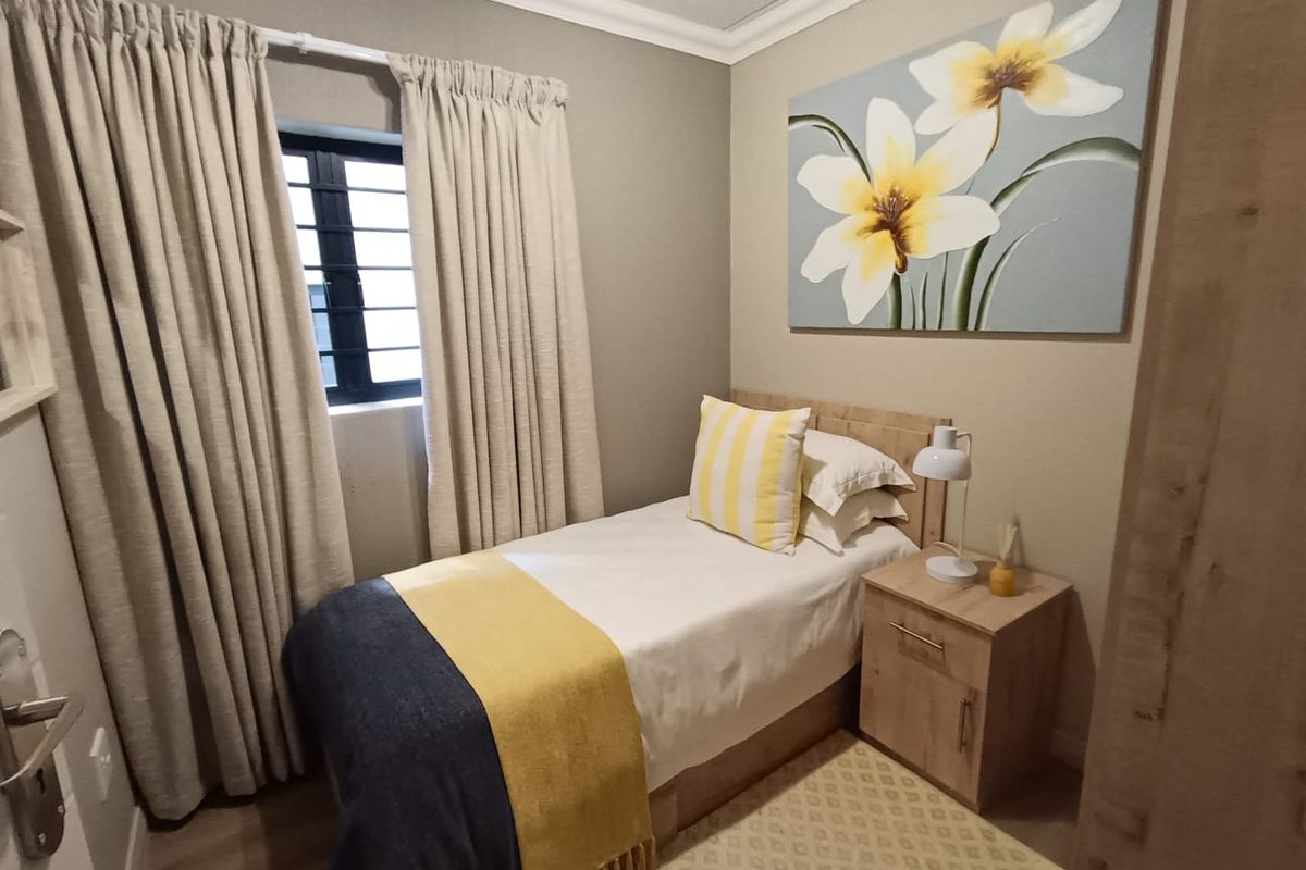 A cozy, well-maintained bedroom featuring neutral wall tones, laminate flooring, and a window with fitted curtain tracks.