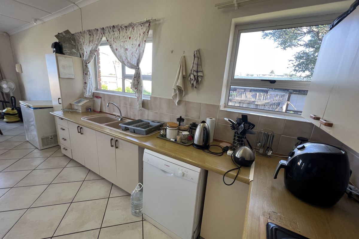 A functional kitchen featuring laminate countertops, a double basin sink, integrated dishwasher space, and tiled flooring with ample natural light.