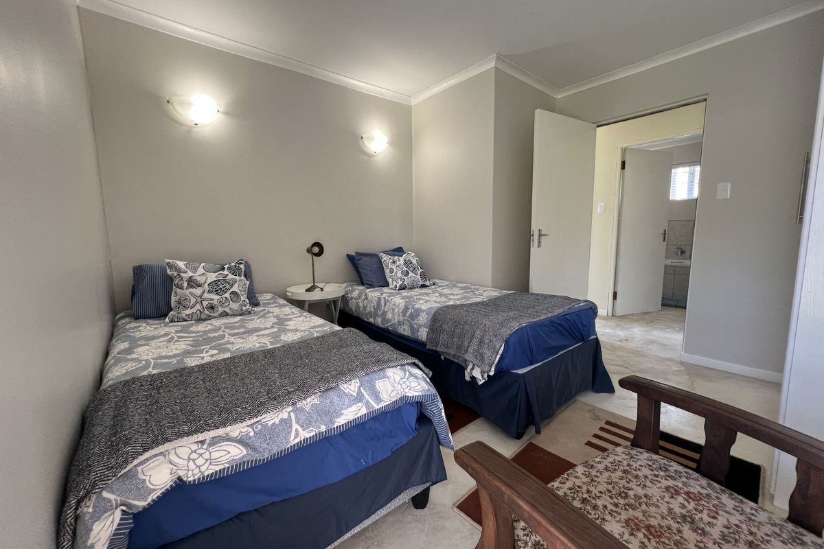 A well-maintained bedroom featuring neutral wall tones, wall-mounted lighting fixtures, and tiled flooring, with an adjacent doorway leading to a bathroom area.